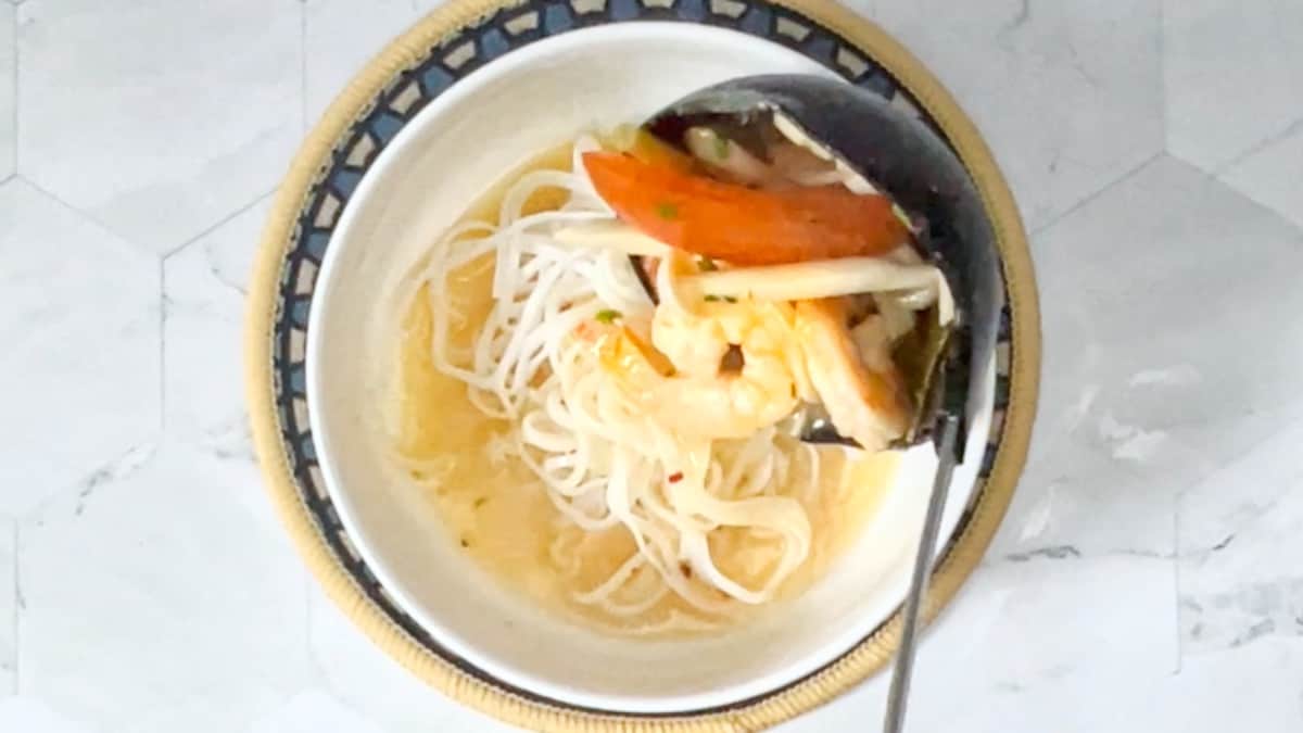 adding tom yum soup to a bowl with cooked noodles