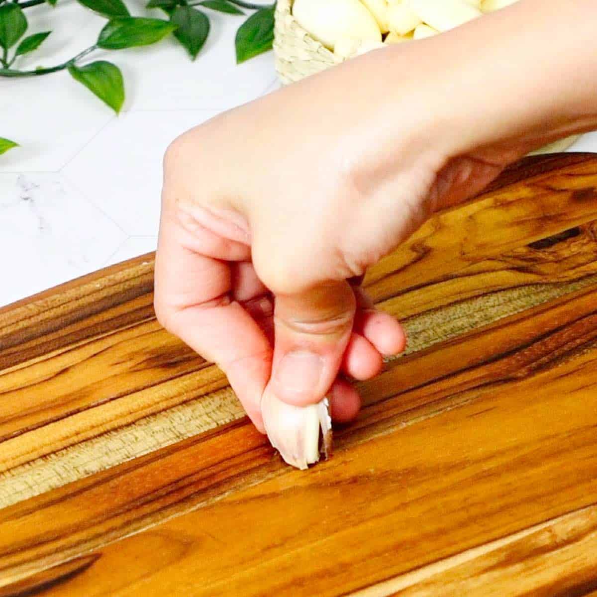 Pushing down the root end of the garlic cloves against a cutting board to crack the peel.