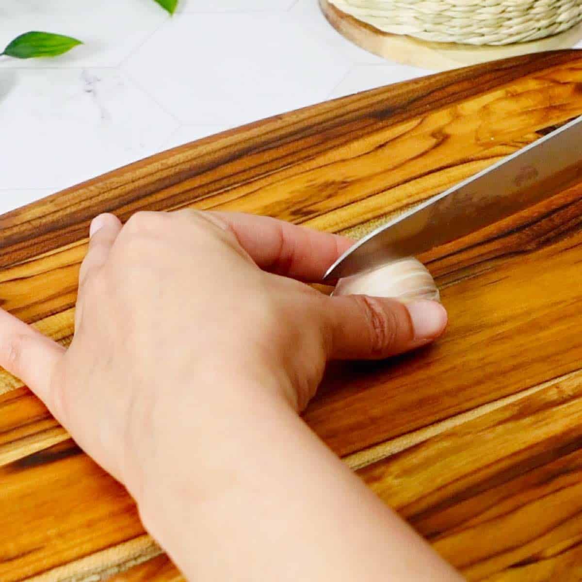 Holding the clove with one hand and placing the sharp edge of the knife on the curved side of the clove.
