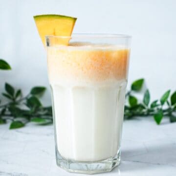 melon milk in a tall glass with a melon wedge on the rim of the glass as garnish