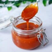 close-up of some honey sriracha sauce dripping from a spoon into a jar full of sauce