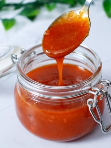 close-up of some honey sriracha sauce dripping from a spoon into a jar full of sauce