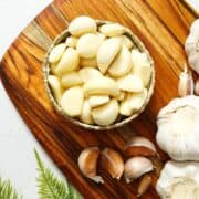 Peeled garlic cloves in a bowl and some garlic bulbs