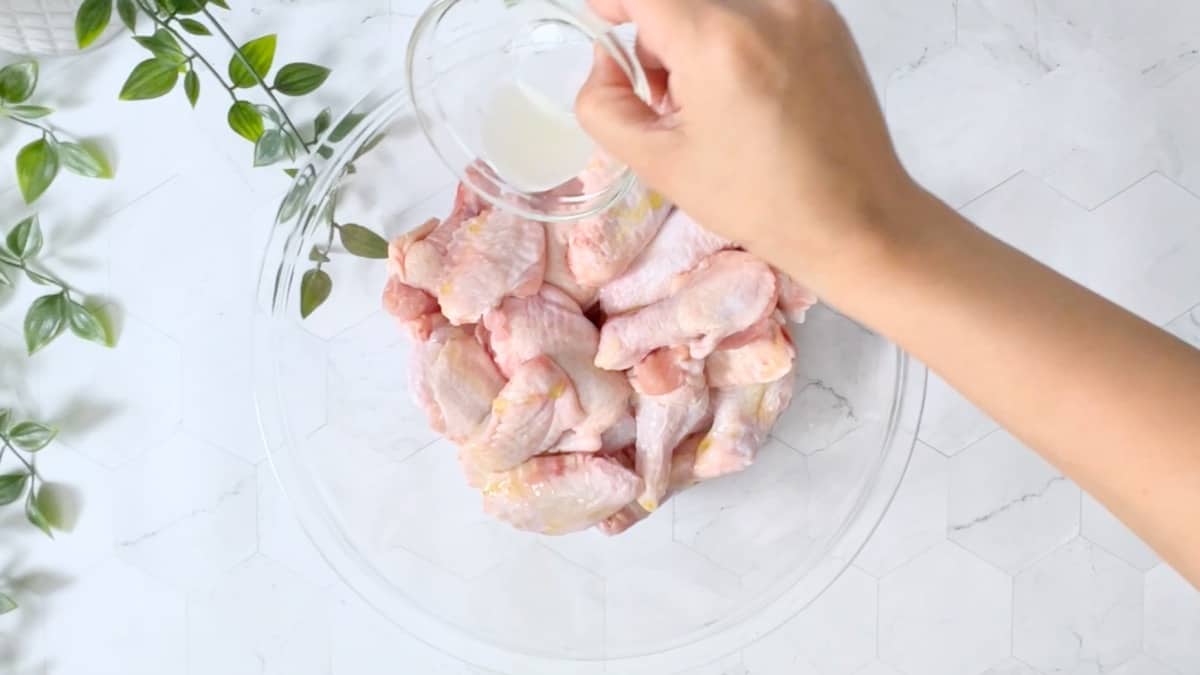 adding lime juice to a bowl of uncooked wings