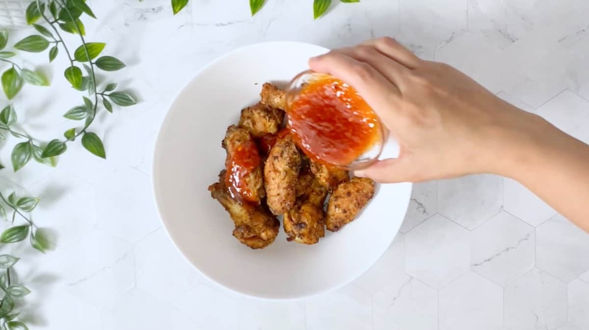adding hot honey sauce to the cooked wings