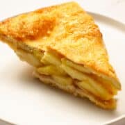 a slice of reheated apple pie with a flaky, golden crust, served on a plate