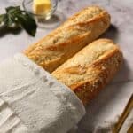 Two softened and reheated baguettes, partially wrapped in a cloth, resting on a table