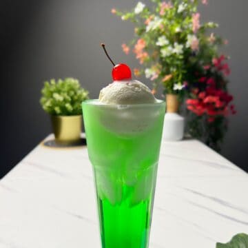 a tall glass of melon soda float with a scoop of vanilla ice cream and a cherry on top