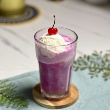 tall glass of purple cow float with some vanilla ice cream and a cherry on top