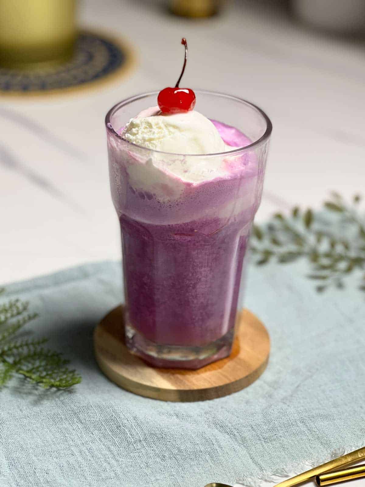 a glass of purple cow float topped with a maraschino cherry