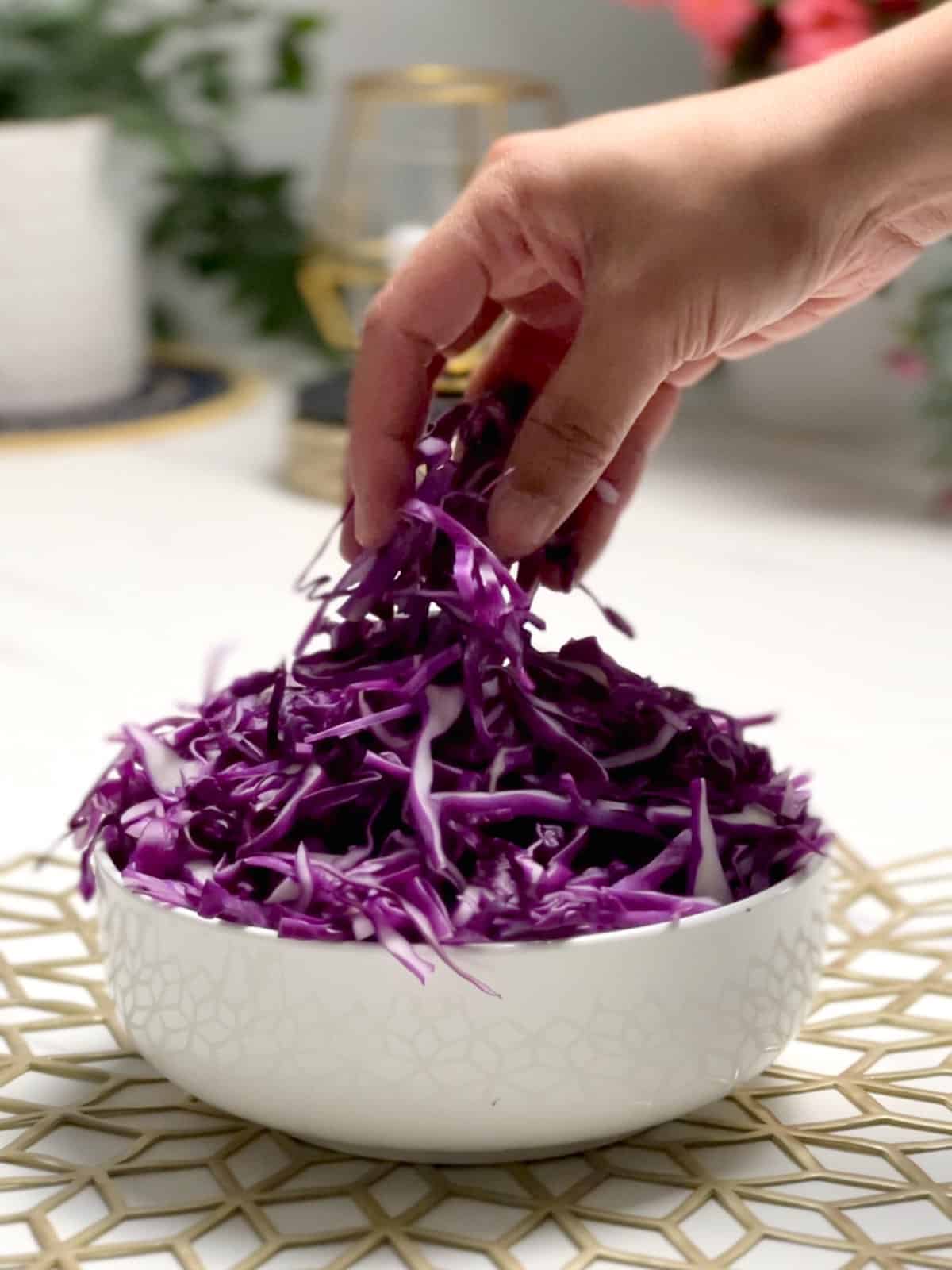 a hand picking up some shredded cabbage from a bowl
