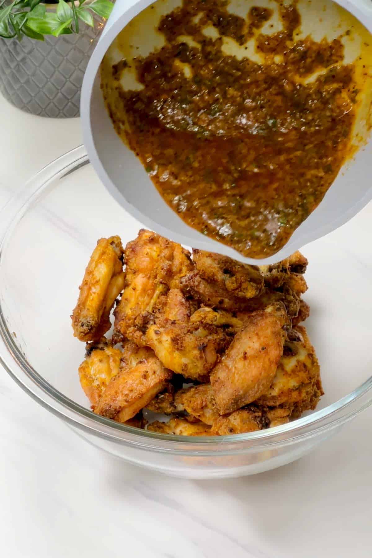 adding garlic pepper sauce to the cooked wings