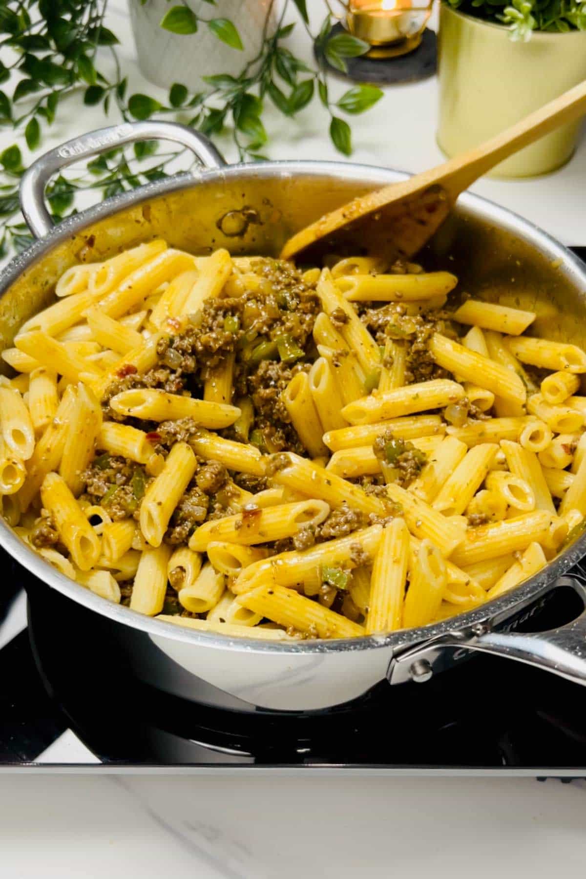 mixing ground beef pesto sauce with cooked pasta