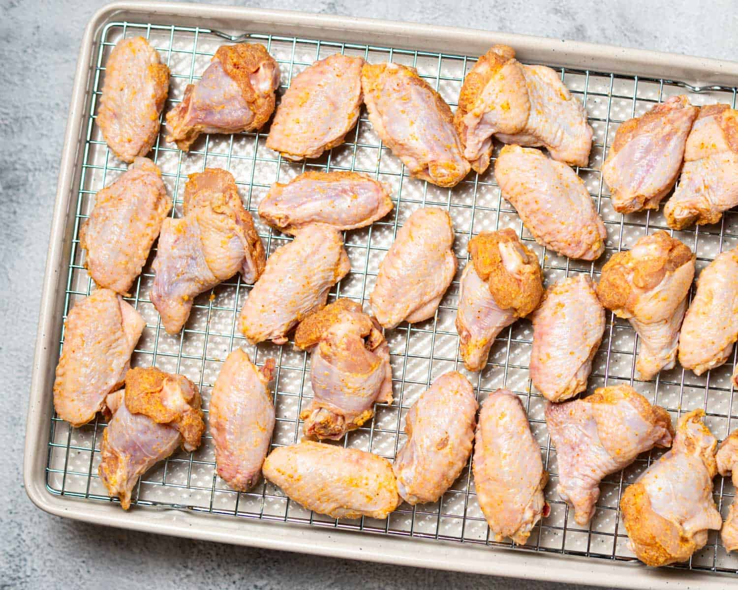 uncooked wings spread out on a wire rack on baking sheet