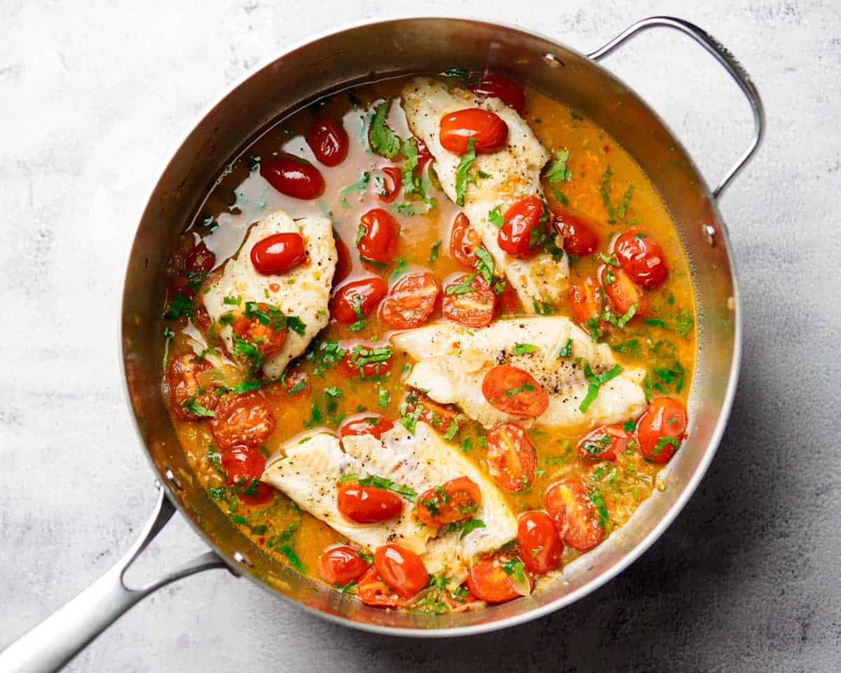haddock fillets cooking in tomato sauce in a skillet