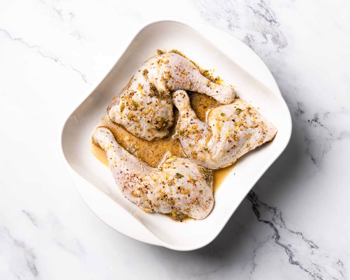 marinated uncooked chicken quarters in a white baking dish