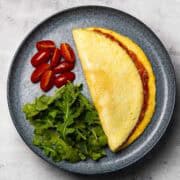 tomato omelette served on a plate with some arugula and tomatoes