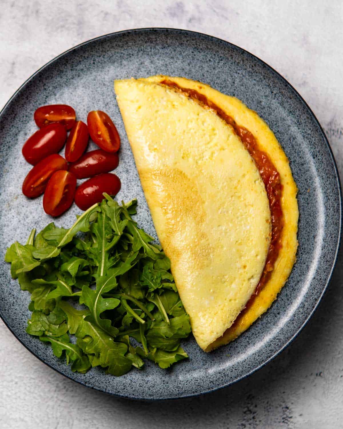 a plate containing tomato omelette, tomatoes, and arugula