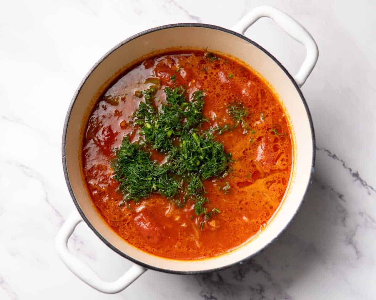 chopped dill and tomatoes cooking in a seasoned soup base in a pot