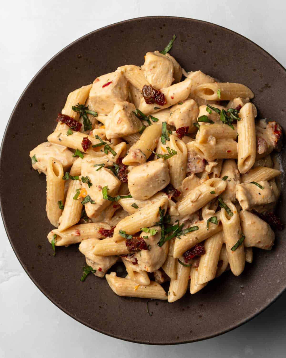 sundried tomato chicken pasta served on a plate topped with basil